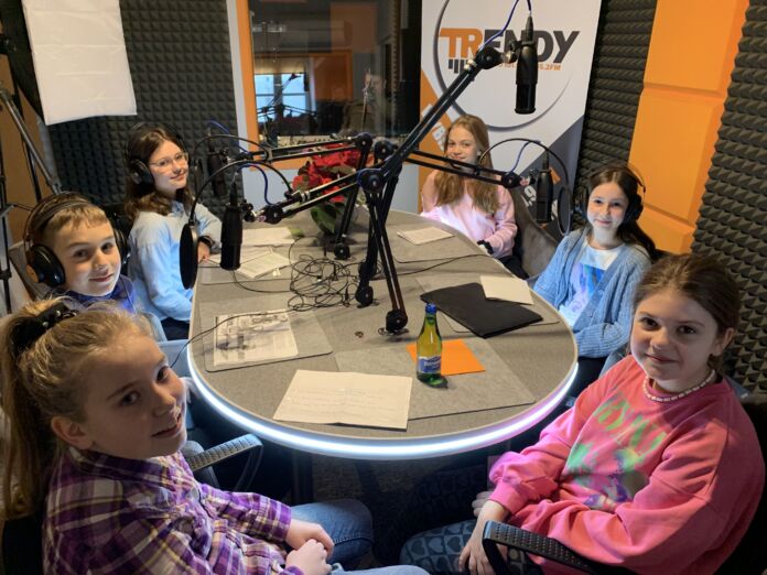 Wizyta w studio radia, stół, mikrofony a przy nim dzieci - zespół projektowy w Radiu Trendy