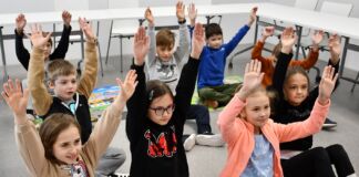 Dzieci siedzące "po turecku" z rękoma u góry
